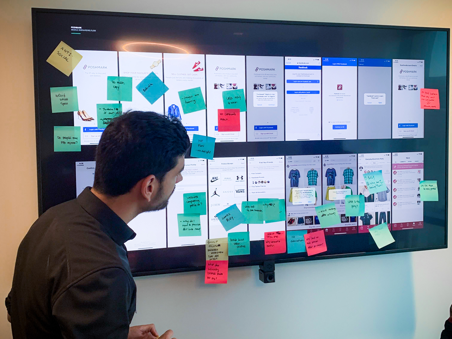 Designer reviewing Poshmark mobile onboarding flow wireframes with sticky note annotations on a large display